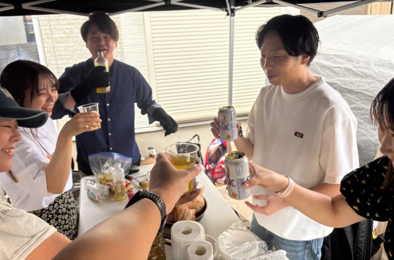 テントの下のテーブルで、グラスと缶を合わせて乾杯するところ