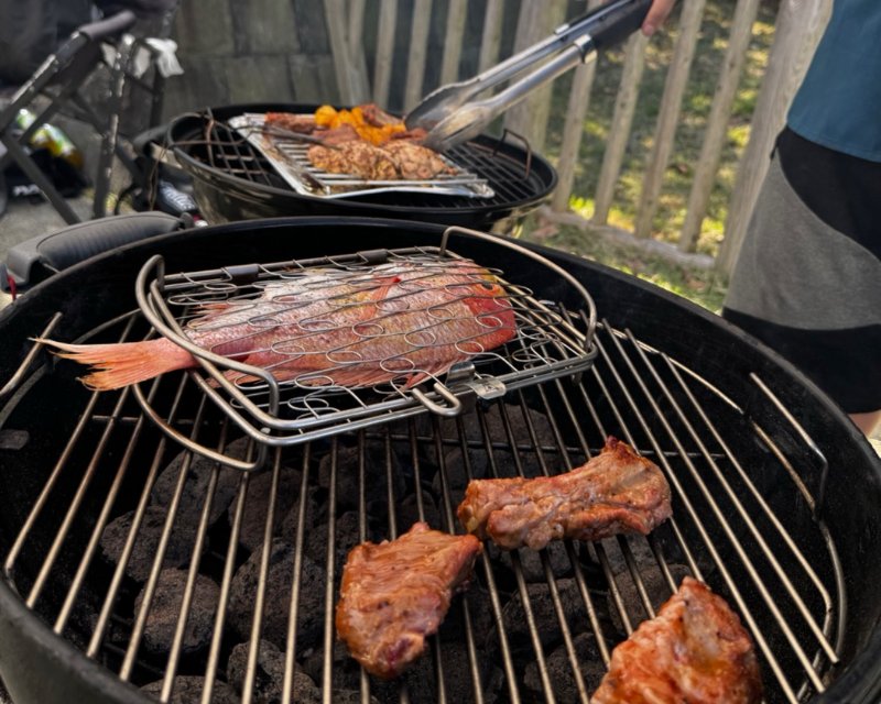 丸いグリルの上で焼かれているスペアリブと、網に挟んだ鯛